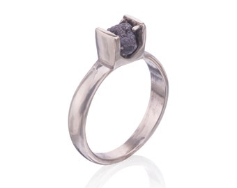 May include: A silver ring with a large, dark gray, rough-cut diamond set in a unique, modern design.