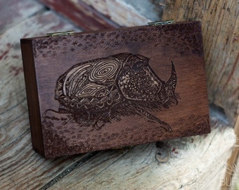 May include: A wooden box with a hinged lid, featuring an intricate laser-engraved design of a beetle with detailed patterns on its shell.