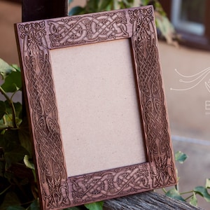 May include: A wooden picture frame with a Celtic knot design carved into the frame. The frame is brown and has a light brown mat.