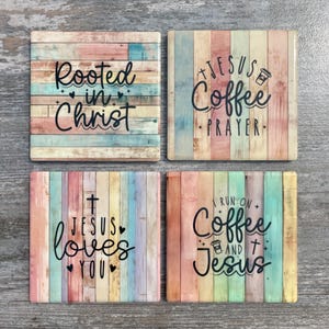 May include: Set of four square coasters with a rustic, pastel wood grain design. Each coaster features a different inspirational quote in black script: "Rooted in Christ," "Jesus Coffee Prayer," "Jesus loves you," and "I run on Coffee and Jesus."