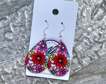 May include: A pair of teardrop-shaped earrings with a floral design. The earrings feature a vibrant pattern of red, pink, purple, yellow, and blue flowers and stripes. The earrings are suspended from silver-colored hooks.