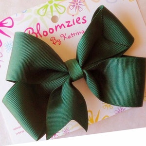 May include: A dark green bow made of grosgrain ribbon. The bow is tied with a knot in the center and has a wired edge. The bow is on a white background with a floral pattern and the text "Bloomzies By Katrina".