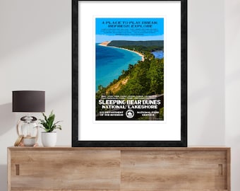 May include: A vintage travel poster for Sleeping Bear Dunes National Lakeshore in Michigan. The poster features a scenic view of a blue lake with a sandy beach and green trees. The text on the poster reads "A place to play, dream, refresh, explore" and "Sleeping Bear Dunes National Lakeshore".