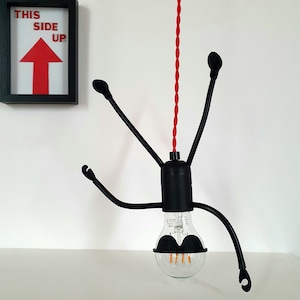 May include: Black pendant light with a red cord and a black bulb. The light fixture has four arms that resemble legs and a bulb with a black mustache.