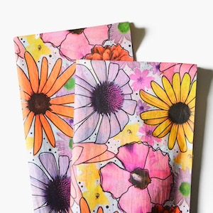 May include: A colorful fabric with a floral pattern. The fabric features a variety of flowers in shades of pink, purple, orange, and yellow. The flowers are outlined in black and have a watercolor effect.