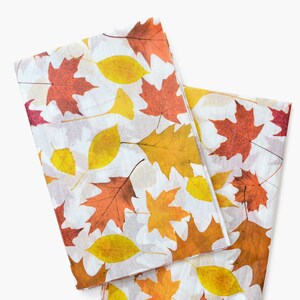 May include: Two pieces of fabric with a white background and a pattern of autumn leaves in shades of red, orange, and yellow.