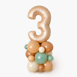 Peut inclure: Un ballon en forme de chiffre trois doré avec un groupe de ballons pastel en beige, crème et vert.