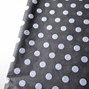 May include: Black tissue paper with white polka dots. The paper is folded in half and the polka dots are visible on both sides.