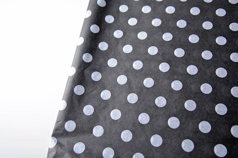 May include: Black tissue paper with white polka dots. The paper is folded in half and the polka dots are visible on both sides.