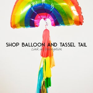 Puede incluir: Globo de aluminio en forma de arco&iacute;ris con una cola de borla. El globo tiene forma de arco&iacute;ris y un acabado brillante. La cola de borla est&aacute; hecha de papel de seda de colores y est&aacute; unida a la parte inferior del globo.