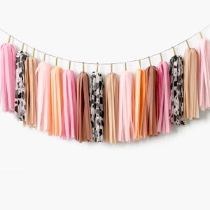 May include: A garland of tissue paper tassels in shades of pink, peach, brown, and black with a leopard print pattern.