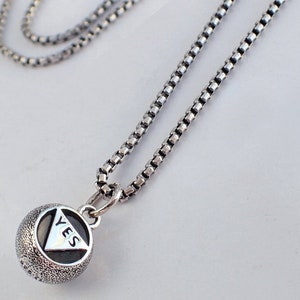 May include: A silver chain necklace with a round pendant that says "YES" in a triangle shape.
