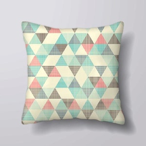 May include: Square cushion featuring a geometric design of triangles in cream, teal, pink, and grey. The triangles form a repeating pattern, offering a contemporary look. The cushion has a soft, textured appearance, suitable for home decor.
