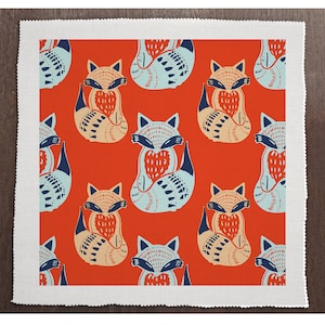 Op de afbeelding: Een rode stof met een herhalend patroon van gestileerde vossen die harten vasthouden. De vossen zijn blauw, oranje en wit.