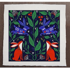 May include: A blue and white patterned fabric with a repeating design of two blue rabbits hopping through a green leafy bush with red berries. Two red rabbits are sitting on either side of the bush, looking up.
