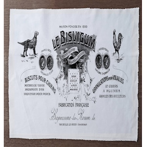 Op de afbeelding: Een witte stof met een vintage ontwerp met de tekst "LE BISVIGUM" en illustraties van een hond en een haan. Het ontwerp bevat Franse tekst en decoratieve elementen, met de woorden "BISCUITS POUR CHIENS" en "GRANULATIONS POUR VOLAILLES".