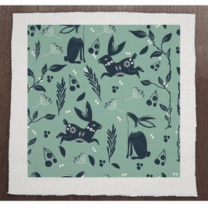 May include: A green fabric with a repeating pattern of black rabbits and white berries. The rabbits are stylized and have a folk art feel.