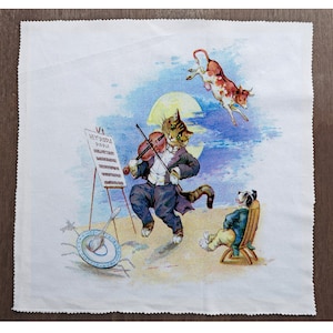 May include: A white tea towel with a colorful illustration of a cat playing the violin, a dog sitting in a chair, and a cow flying in the air. The cat is wearing a tuxedo and holding a violin. The dog is wearing a blue and white striped shirt. The cow is brown and white. The illustration is set against a blue sky with a full moon.