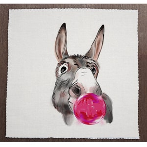 以下が含まれることがあります： 大きな鮮やかなピンク色のシャボン玉を吹いているロバの気まぐれなイラスト。ロバの顔は、白の背景に対して、グレー、ブラウン、ピンクの色合いで詳細に描かれています。このアートワークは、正方形のテクスチャード加工された生地にあります。