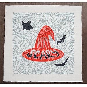 May include: A red witch's hat with the words "Very Scary" written on it. The hat is surrounded by a blue and white swirling pattern with a ghost and bats.