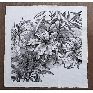 May include: Black and white illustration of lilies with detailed petals and leaves. The lilies are arranged in a cluster, with some overlapping. The image is printed on a white fabric background.