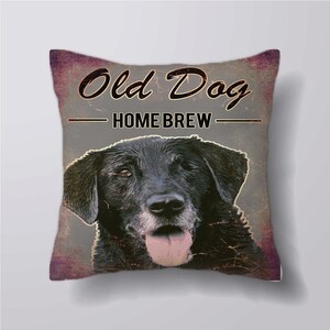 May include: A gray and purple pillow with a black Labrador Retriever dog on it. The dog has a pink tongue sticking out. The pillow has the text "Old Dog - Home Brew" on it.