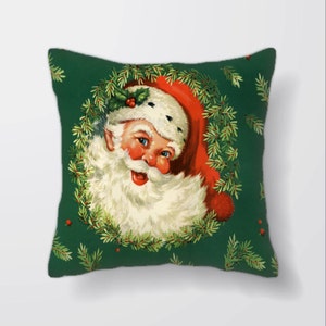 Puede incluir: Una almohada verde con una ilustración vintage de la cara de Santa Claus enmarcada por una corona de acebo y ramas de pino.