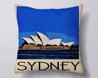 May include: A blue and white throw pillow with a vintage-style illustration of the Sydney Opera House and the word "SYDNEY" printed in black.
