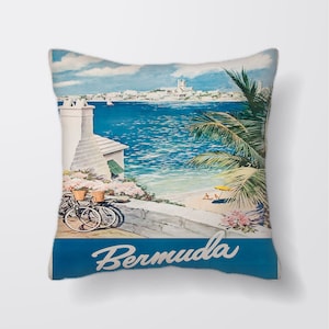 Puede incluir: Una almohada de estilo póster de viaje vintage con una ilustración colorida de una ciudad costera con una palmera, un edificio blanco con una chimenea y dos bicicletas. El texto "Bermuda" está escrito en una fuente cursiva en la parte inferior de la almohada.