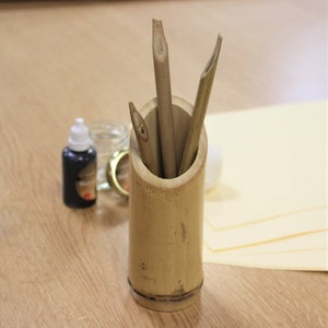 May include: A bamboo pen holder with three bamboo calligraphy pens inside. The holder is on a wooden surface with a bottle of black ink and a jar.