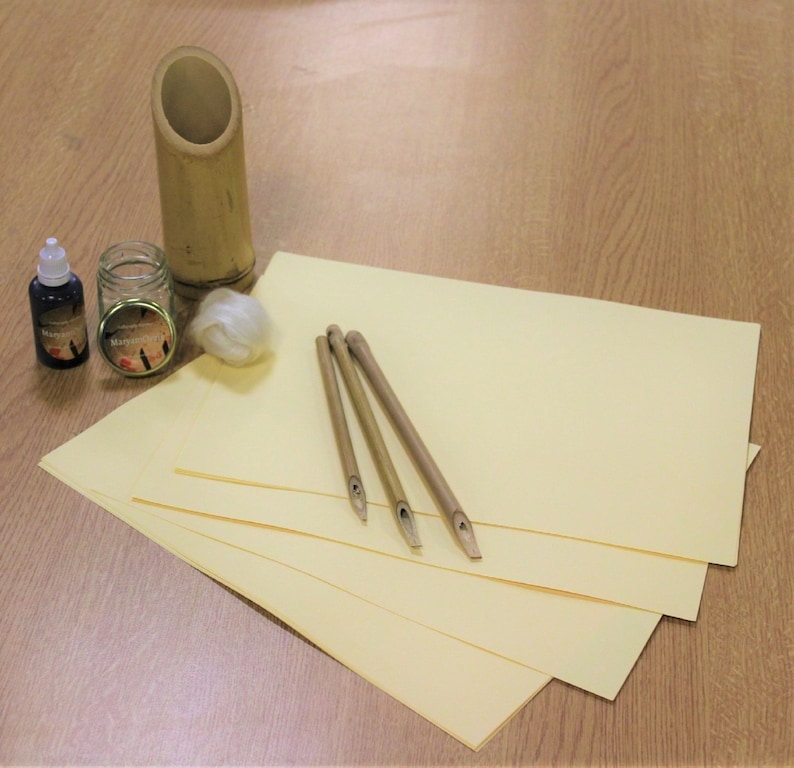 May include: A set of calligraphy supplies including four bamboo dip pens, a bamboo pen holder, two bottles of black ink, a small jar of ink, and a piece of white cotton. The supplies are arranged on a light brown wooden surface.