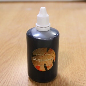 May include: A small bottle of black calligraphy ink with a white cap. The label reads "Calligraphy Supplies MaryamOvais".