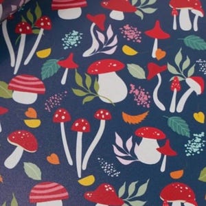 May include: Dark blue background with a repeating pattern of red and white mushrooms, green leaves, and small pink and yellow floral accents. The mushrooms have white stems and red caps with white spots.