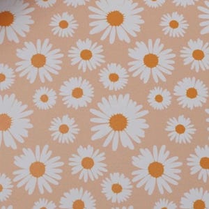 May include: A repeating pattern of white daisies with orange centers on a peach-colored background. The flowers vary in size, creating a dynamic and visually appealing design. This floral pattern is suitable for various applications.