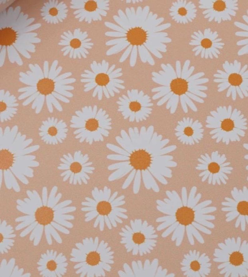 May include: A repeating pattern of white daisies with orange centers on a peach-colored background. The flowers vary in size, creating a dynamic and visually appealing design. This floral pattern is suitable for various applications.
