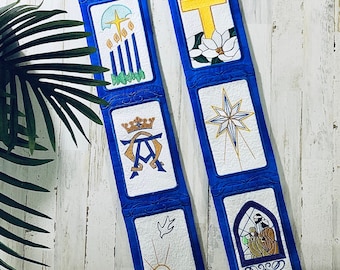 May include: A blue fabric stole with embroidered images of a cross, a star, a dove, a manger, a crown, and candles. The stole is decorated with gold and white embroidery.