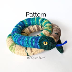 May include: A crocheted snake toy with a blue, green, and beige color scheme. The snake has a yellow eye and a blue tongue. The toy is coiled in a circle and the text "Pattern" is above the toy. The text "cbfiberworks.com" is below the toy.