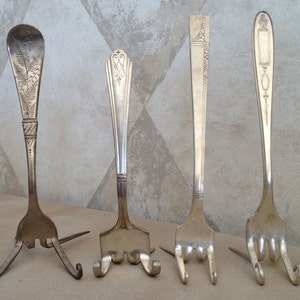 May include: Four silver forks have been bent into a tripod shape to create a display stand for small items. The forks have decorative designs on the handles.