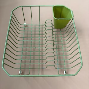 May include: A light green wire dish rack with a matching utensil holder. The rack is square with a grid pattern and has a small, attached cup for utensils. The dish rack is made of metal.