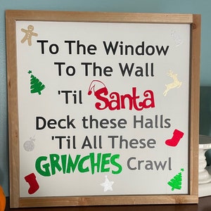 May include: A white wooden sign with a Christmas-themed saying: "To the window, to the wall, 'til Santa. Deck these halls 'til all these Grinches crawl."
