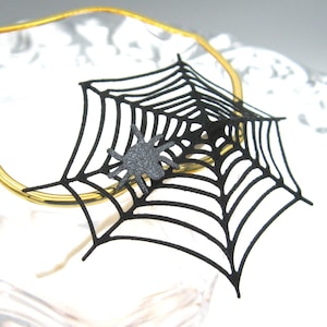 May include: Black spider web with a black spider in the center, on a clear glass with a gold rim.