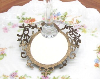 May include: Gold-colored metal wine glass charm with a circular place card holder and a decorative filigree design.