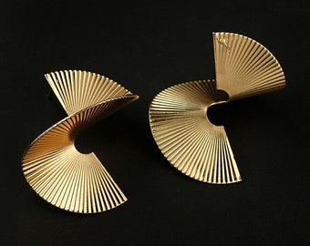 May include: A pair of gold-toned geometric earrings with a spiral design. The earrings are made of metal and have a fan-like shape.