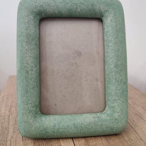 May include: A rectangular picture frame with rounded corners and a textured, sage green finish. The frame features a thick, chunky border surrounding a plain, light gray rectangular insert, presenting a solid and uniform appearance throughout.