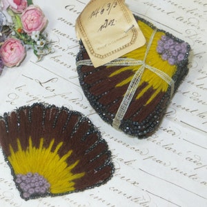 May include: Two vintage, fan-shaped textile embellishments. One is a stack of pieces, the other is a single piece. They feature brown, yellow, and purple embroidery with beaded edges. A tag reads "MADE IN GERMANY".
