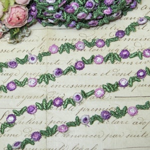 May include: A close-up of a green and purple floral trim with small flowers and leaves. The trim is on a piece of paper with French text.
