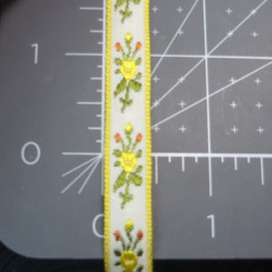 May include: A white ribbon with a yellow border and a repeating pattern of green leaves and yellow flowers with orange centers.