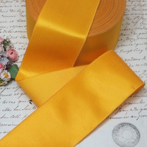 May include: A roll of bright yellow satin ribbon. The ribbon is folded and displayed on a piece of paper with handwritten text.