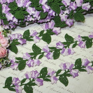 May include: Purple and green floral lace trim with a delicate design of bell-shaped flowers and leaves.