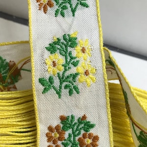 May include: White ribbon with a yellow fringe and a repeating pattern of embroidered yellow, orange, and green flowers.